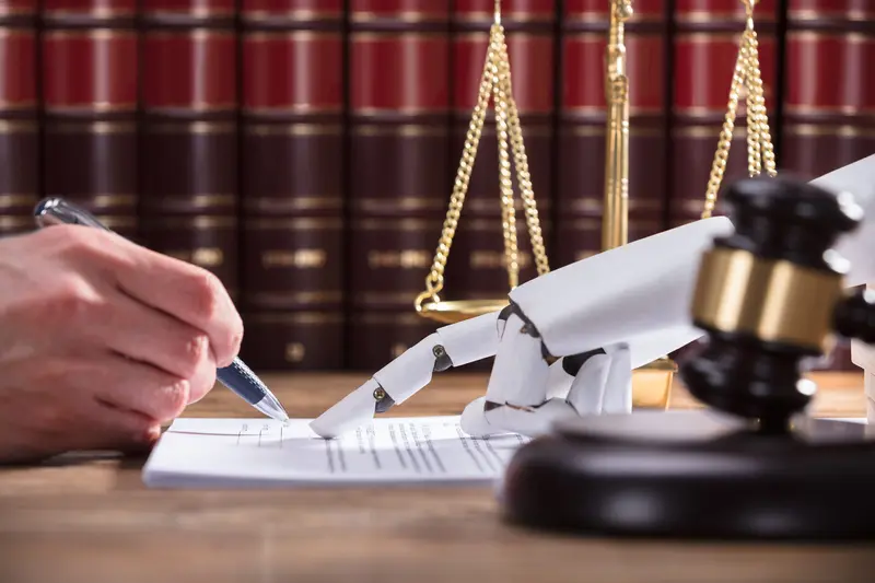 A robotic hand signing a document beside scales of justice and a judge's gavel